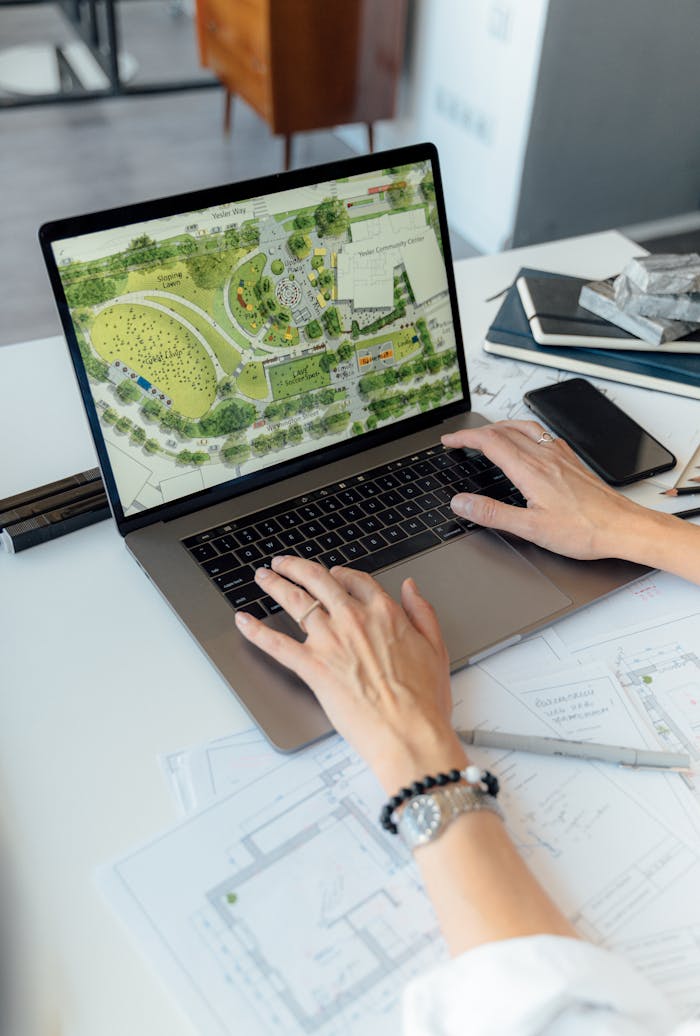 Architect working on landscape plan displayed on laptop with hands typing on keyboard.